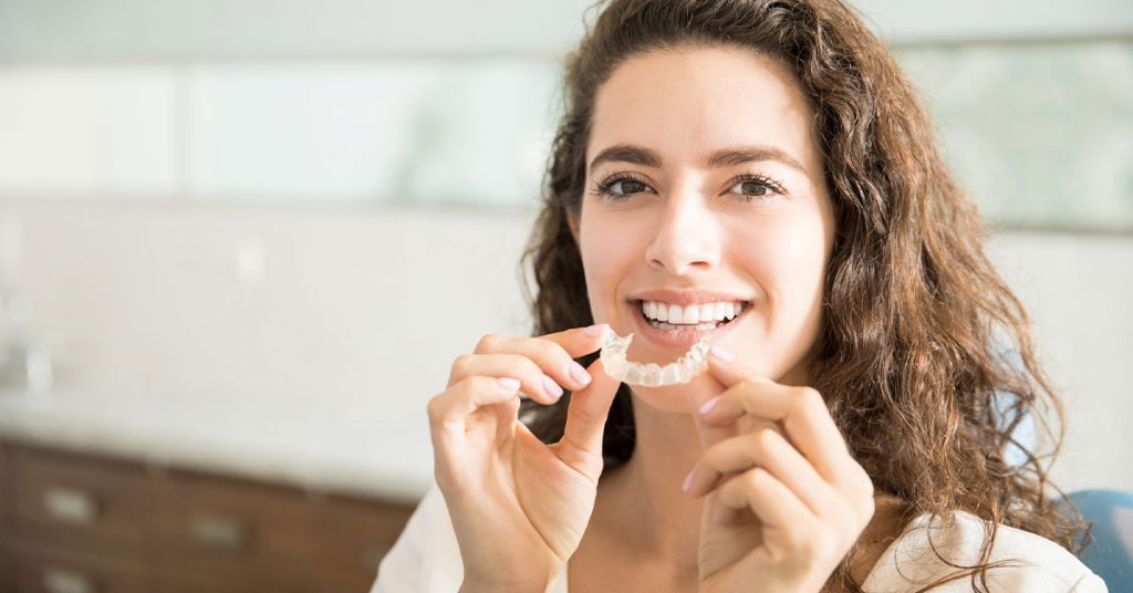 Dental invisible braces or silicone trainer in the hands of a young smiling girl. Orthodontic concept - Clear braces